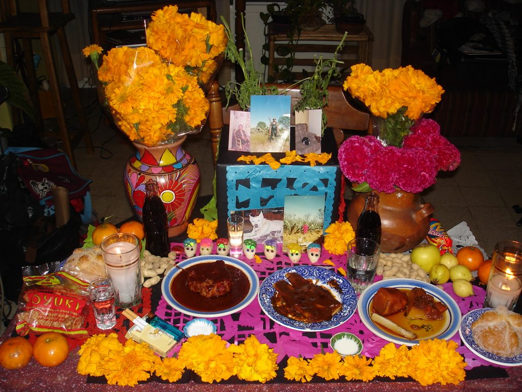 A Day of Dead altar with offerings of food and drink and candles and sugar skulls.