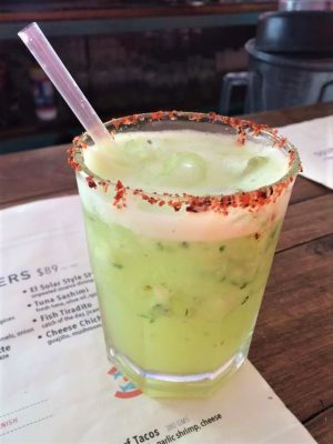 A glass with cucumber jalepeno cocktail, ice, and chile salt on the rim .