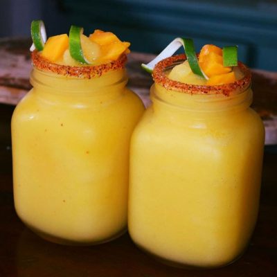 Two glasses of mango margaritas with fresh fruit on top.