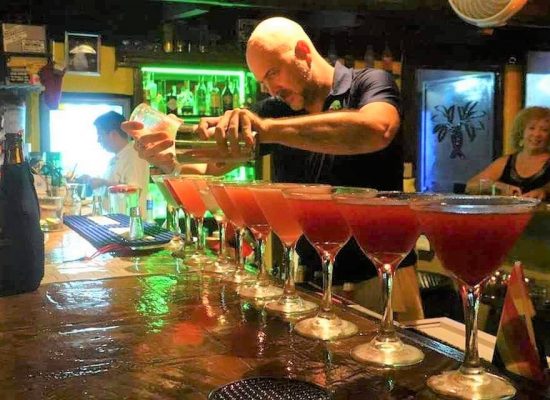 Bartender mixing a row of colorful martinis. 