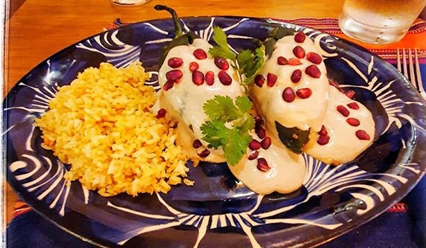 Two stuffed chiles en nogado sauce and rice on a blue plate.