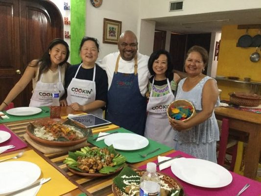 Chef Enrique gathers around a table of food with his students. 