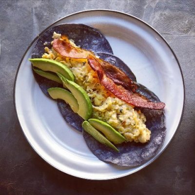 scrambled eggs, avacado slices and bacon on three blue corn tortillas. 